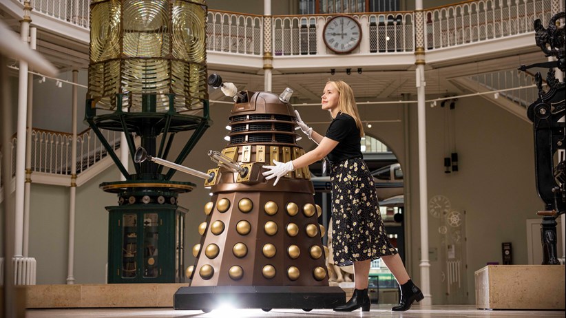 A woman in the National Museum of Scotland pushing a Dalek from Doctor Who across the museum floor. © Duncan McGlynn
